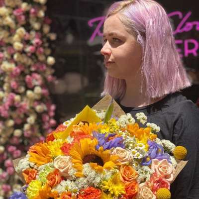 Person holding a colorful bouquet with sunflowers, roses, and purple flowers