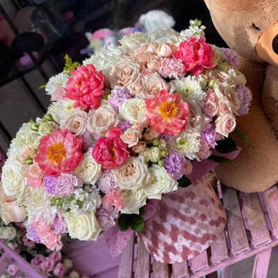 Large pastel bouquet with pink, white, and lavender flowers beside a teddy bear