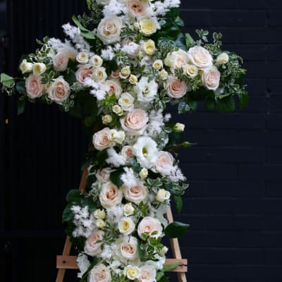 Cross-shaped floral tribute with pale roses and white blooms on an easel