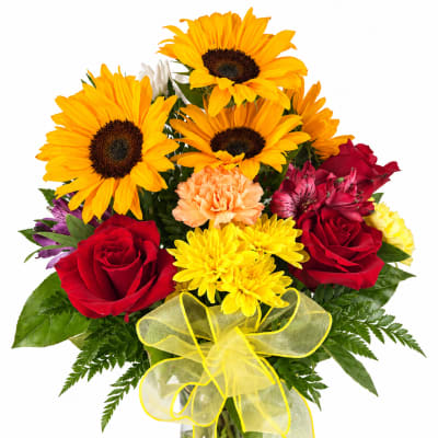 Bouquet of sunflowers, red roses, and mixed blooms in a glass vase with a yellow ribbon