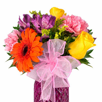 Colorful bouquet of mixed flowers in a purple vase with a pink ribbon