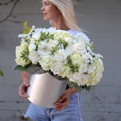 Woman holding a large white floral arrangement in a silver vase