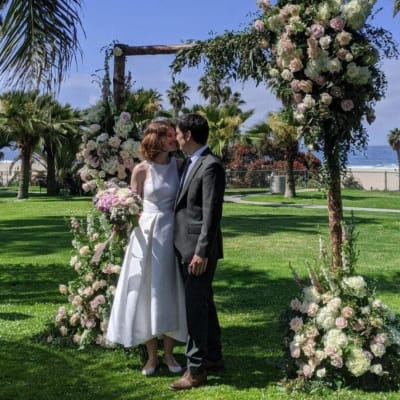 Bride and groom standing under a floral wedding arch by the beach