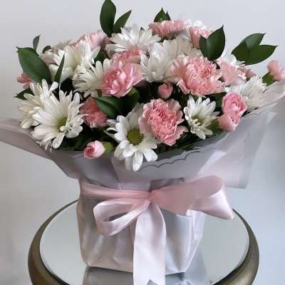 Pink carnations and white daisies in a wrapped bouquet with a pink ribbon