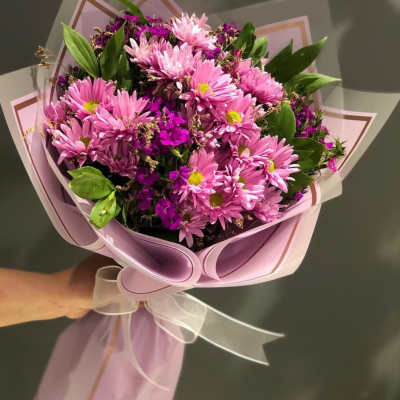 Pink daisy bouquet wrapped in pastel paper with a white ribbon