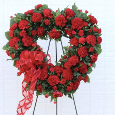Heart-shaped wreath of red carnations on a stand with a red ribbon bow