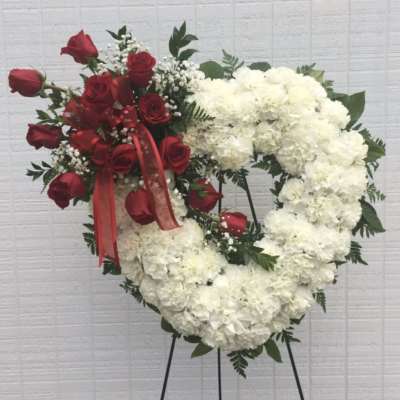 Heart-shaped floral wreath with red roses and white flowers on a stand