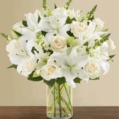 White lilies and cream roses arranged in a clear glass vase
