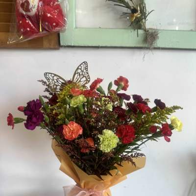 Mixed bouquet of colorful carnations wrapped in gold paper with a pink bow