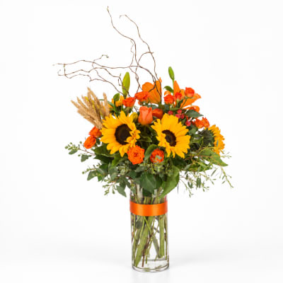 Sunflowers and orange roses in a clear glass vase with branches