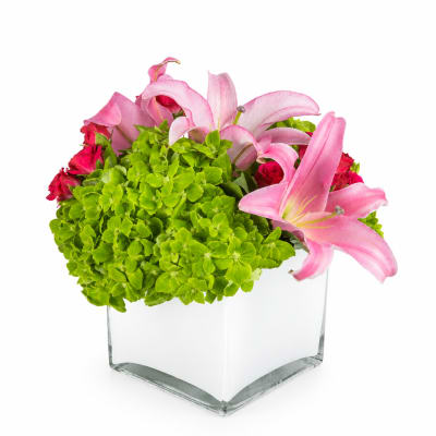 Pink lilies and roses with bright green hydrangeas in a clear square vase