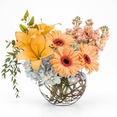 Orange lilies and gerbera daisies in a clear glass vase
