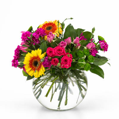 Mixed bouquet of pink roses, yellow gerberas, and purple flowers in a glass vase