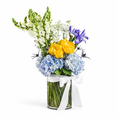Bouquet of yellow roses, blue hydrangeas, and purple irises in a glass vase