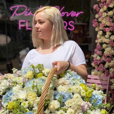 Woman holding a large basket of pastel flowers outside a flower shop