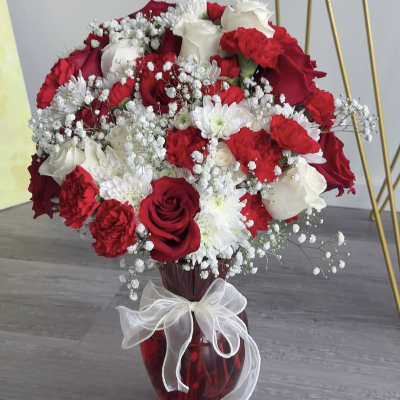 Red and white rose bouquet in a red glass vase with a white ribbon
