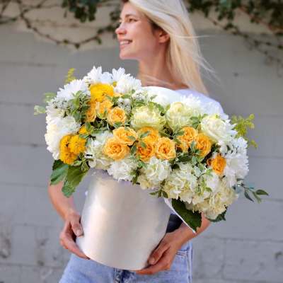 Woman holding a large bouquet of white and yellow flowers in a silver box