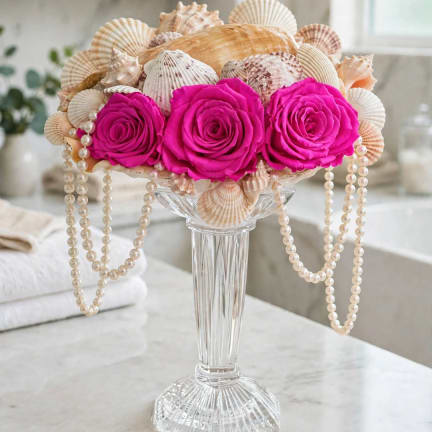 Pink roses in a clear vase with seashells and pearl strands