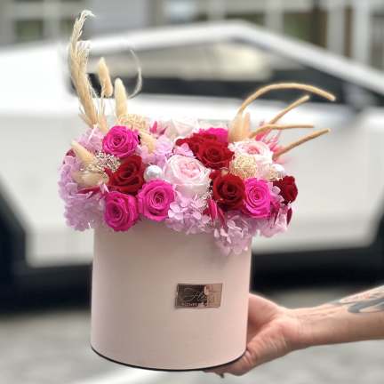 Pink and red roses arranged in a round hatbox with dried accents.