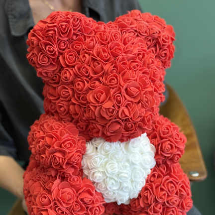 Red teddy bear made of rose-shaped flowers with a white heart on its chest