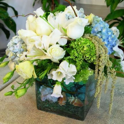 White and blue floral arrangement in a square glass vase
