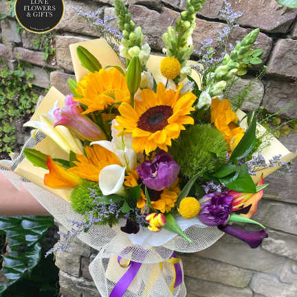Bright mixed bouquet with sunflowers, lilies, snapdragons and purple blooms wrapped in mesh with ribbons.