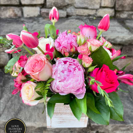 Pink and white peonies, roses, tulips, and other blooms in a whitewashed wood cube vase.