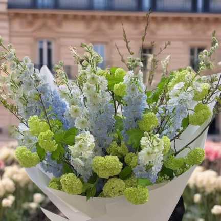 Bouquet of pale blue and white flowers with lime-green blooms wrapped in white paper