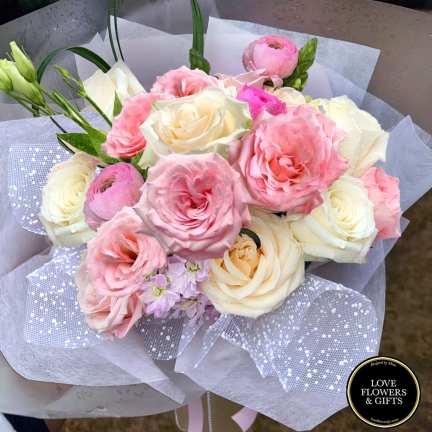Hand-tied bouquet of pink and cream roses with ranunculus wrapped in white and dotted mesh paper