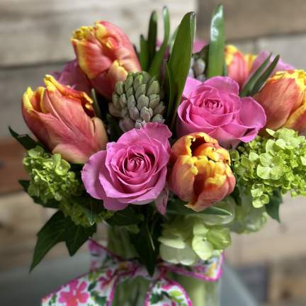 Bright bouquet of pink roses, orange-yellow tulips, and green hydrangeas in a glass vase with a floral bow
