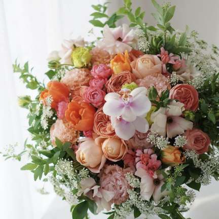 Round bouquet of peach, pink, and white flowers with greenery