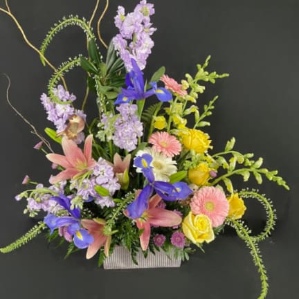 Mixed bouquet with pink lilies, blue irises, and yellow roses in a rectangular vase