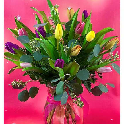 Vase of mixed-color tulips with lush foliage and ribbon on a bright pink background