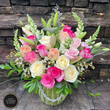 Mixed bouquet of pink, peach, and cream roses with lilies and snapdragons in a green vase