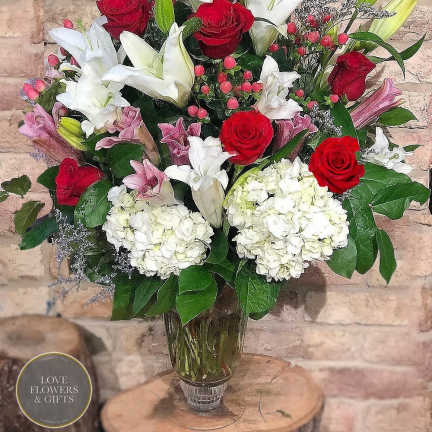 Tall bouquet of red roses, white and pink lilies, and white hydrangeas in a clear glass vase
