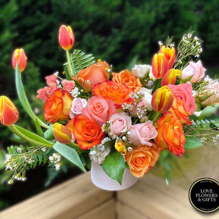 Arrangement of orange and pink roses with yellow-orange tulips in a white vase