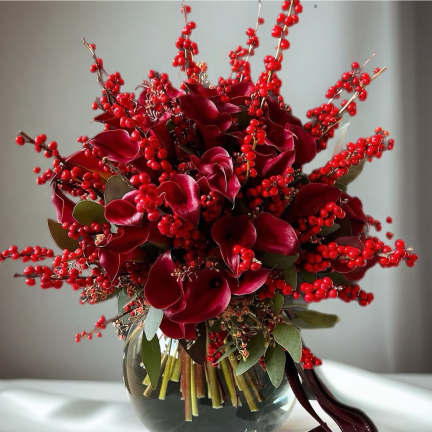 Deep red floral arrangement in a glass vase with berry branches and ribbon