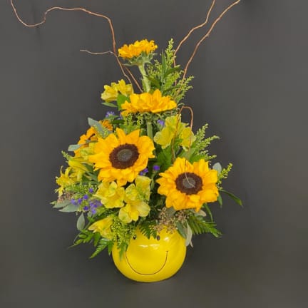 Sunflower arrangement in a yellow smiley-face vase with curly branches