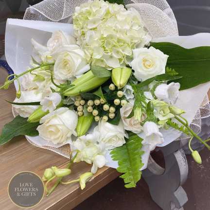 Hand-tied bouquet of white roses, lilies, orchids, and hydrangea wrapped in white mesh and paper