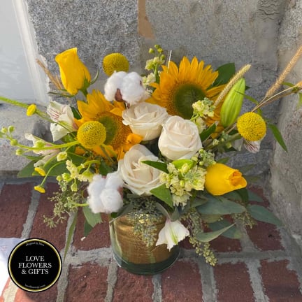 Vase arrangement of yellow sunflowers, white roses, and yellow tulips in a glass cylinder vase