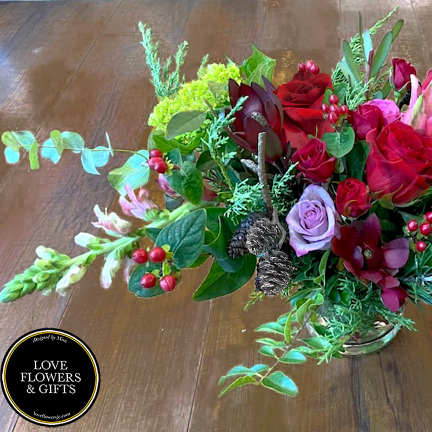 Low centerpiece of red roses, pink lilies, berries, and pine cones in a clear glass vase
