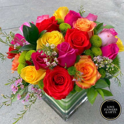 Bright mixed rose arrangement with green button mums in a clear glass cube vase