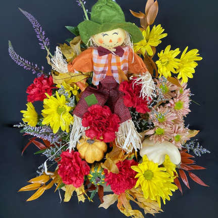 Scarecrow decoration surrounded by yellow, red, and pink flowers