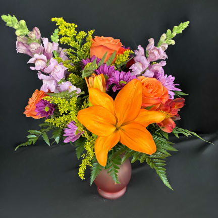 Colorful bouquet with orange lilies, roses, and purple flowers in a frosted vase