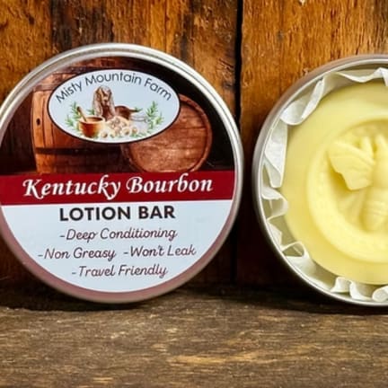 Two round tins of lotion bar on a wooden surface, one labeled Kentucky Bourbon.