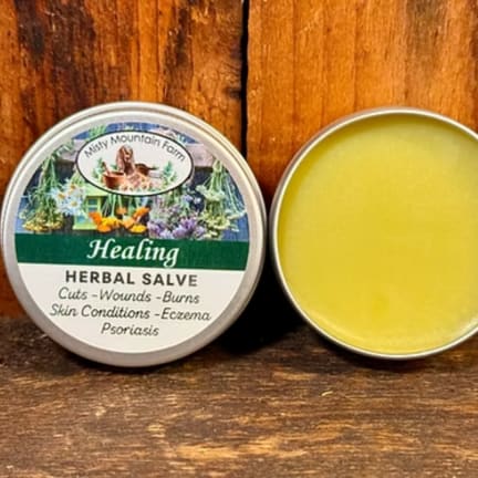 Two tins of herbal salve on a wooden surface, one open with yellow balm