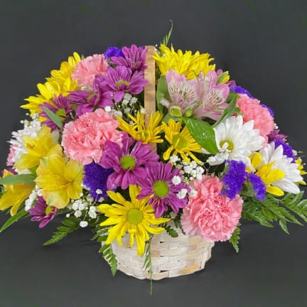 Mixed bouquet of yellow, purple, pink, and white flowers in a woven basket
