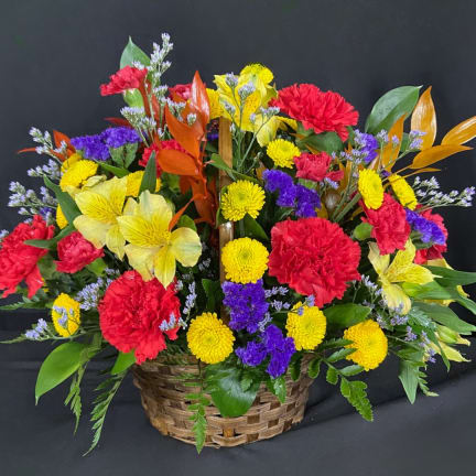 Colorful mixed flower basket with red carnations, yellow mums, and purple filler flowers