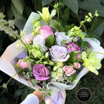 Handheld bouquet of pastel roses and pale yellow flowers wrapped in white paper