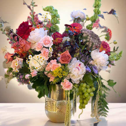 Large mixed floral arrangement in a gold vase with pink, white, and green blooms